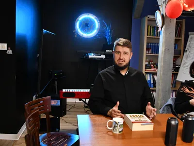Ksiądz Łukasz prowadzi spotkanie Drużyny Pasterza o stereotypach zacofania wierzących, w tle niebieski neon i czerwone balony w DomSpocie Ostrów.
