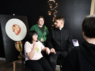 Trójka osób w strefie chilloutu DomSpotu, w tle obraz z sercem i kielichem. Chwila oddechu przed spotkaniem o wątpliwościach duchowych.