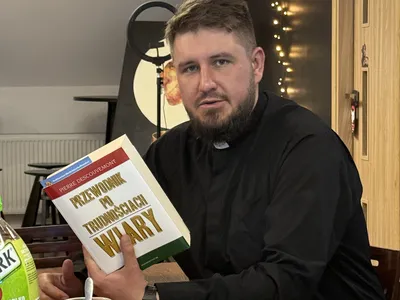 Ksiądz Łukasz Urban z uśmiechem prezentuje książkę Pierre Descouvemont „Przewodnik po trudnościach wiary” podczas spotkania młodzieży w DomSpocie Ostrów.